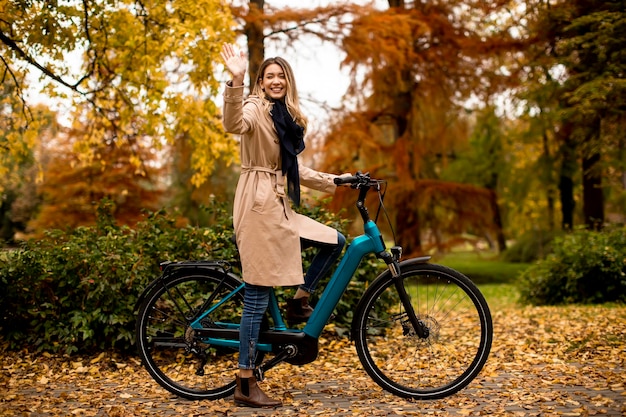 Giovane donna con la bicicletta elettrica nel parco autunnale di te