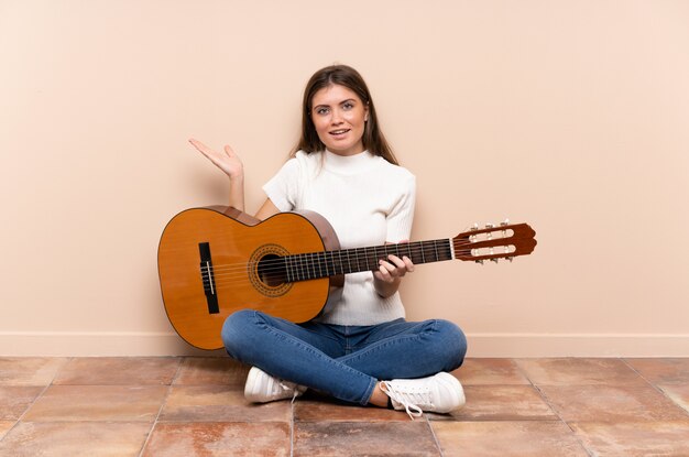 Giovane donna con la chitarra che si siede sul copyspace della tenuta del pavimento immaginario sulla palma