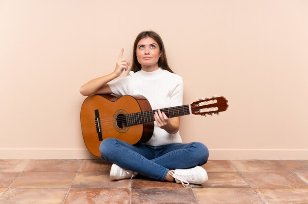 Giovane donna con la chitarra che si siede sul pavimento che indica con il dito indice una grande idea