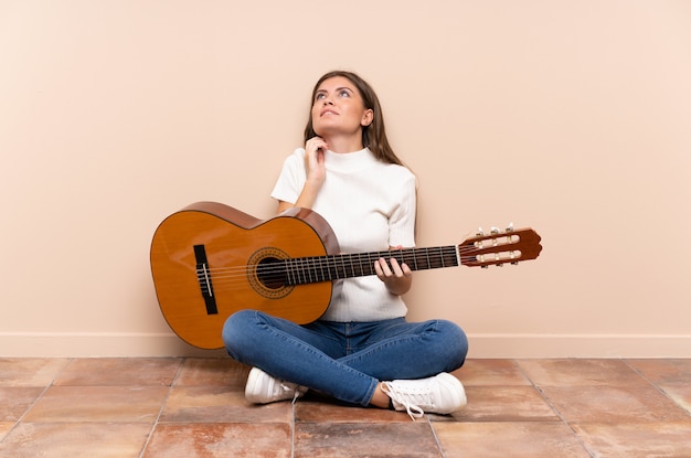 Giovane donna con la chitarra che si siede sul pavimento che pensa un'idea