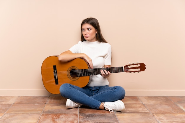 Giovane donna con la chitarra che si siede sul pavimento che pensa un'idea