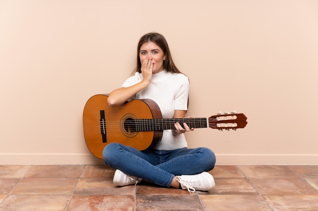 Giovane donna con la chitarra che si siede sul pavimento con espressione facciale di sorpresa