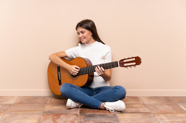 Giovane donna con la chitarra che si siede sulla risata del pavimento