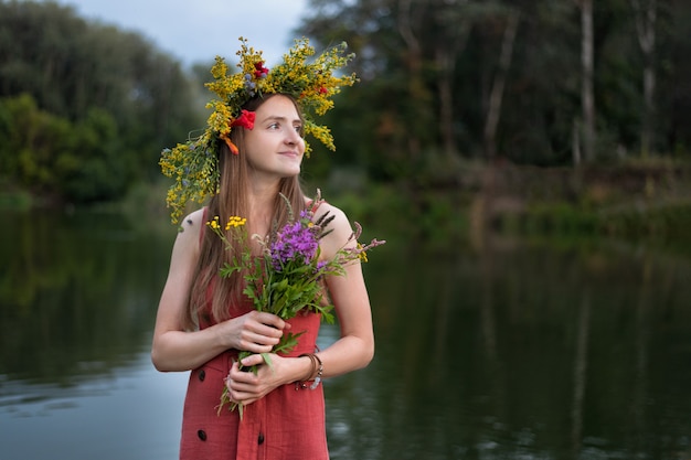 Giovane donna con la corona sulla testa di fiori di campo sullo sfondo del lago.