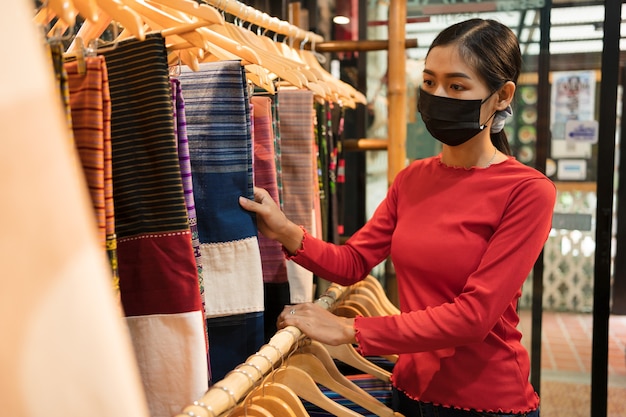 Giovane donna con la maschera in negozio guardando i vestiti