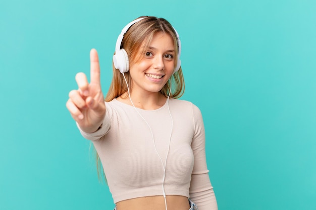 Giovane donna con le cuffie che sorride con orgoglio e sicurezza facendo il numero uno