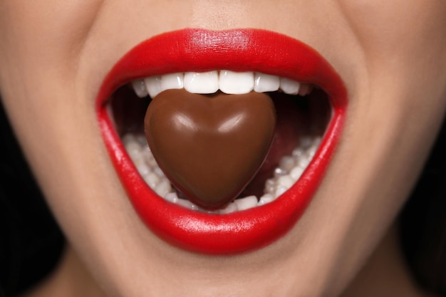 Giovane donna con le labbra rosse che mangia il primo piano della caramella di cioccolato a forma di cuore