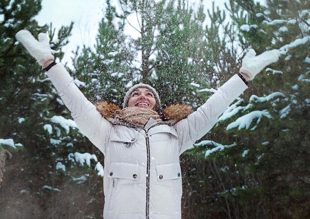 Giovane donna con le mani alzate nella foresta invernale Donna che lancia neve con le mani