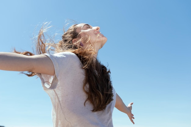 Giovane donna con le mani estese che respirano isolata sul cielo blu.