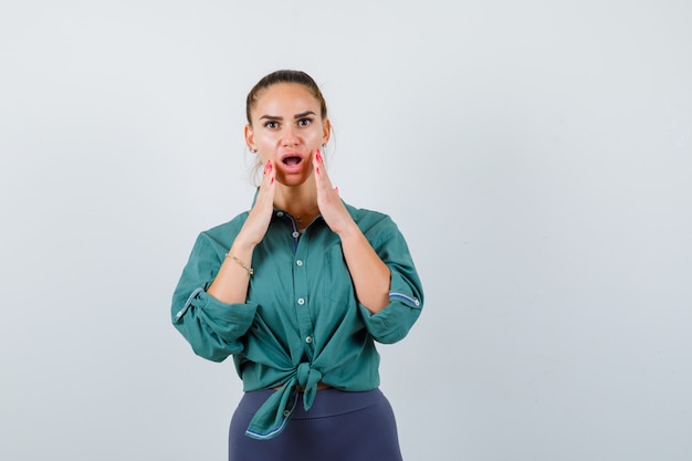 Giovane donna con le mani vicino alla bocca aperta in camicia verde e sembra scioccata. vista frontale.