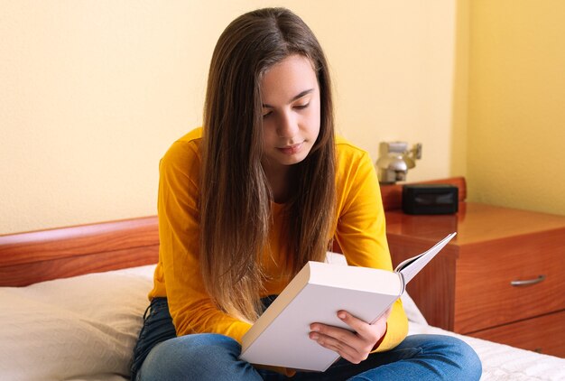 Giovane donna con lettura seduta sul letto