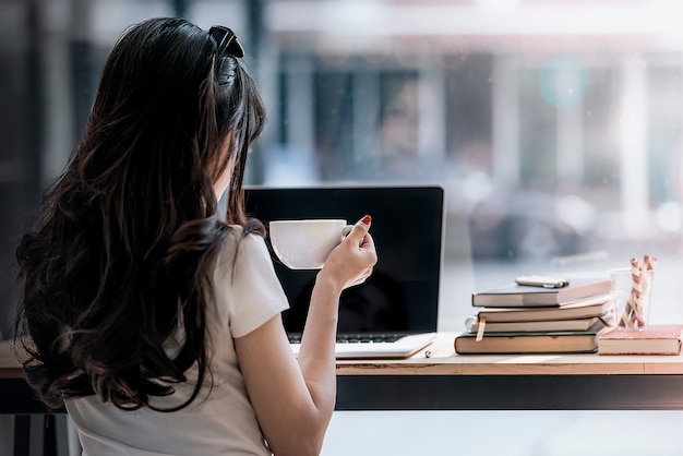 giovane donna con lunghi capelli neri con caffè e lavorando con computer portatile al caffè