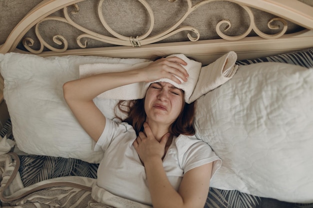 Giovane donna con mal di testa influenza malata malattia fredda a casa coperta sdraiata sul letto con impacco freddo sulla testa in camera da letto a casa
