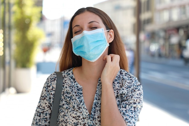 Giovane donna con maschera chirurgica prurito sintomi di allergia grattandosi il collo in una strada cittadina