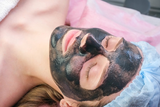 Giovane donna con nanogel di carbonio sul viso in salone. Procedura di pelatura.
