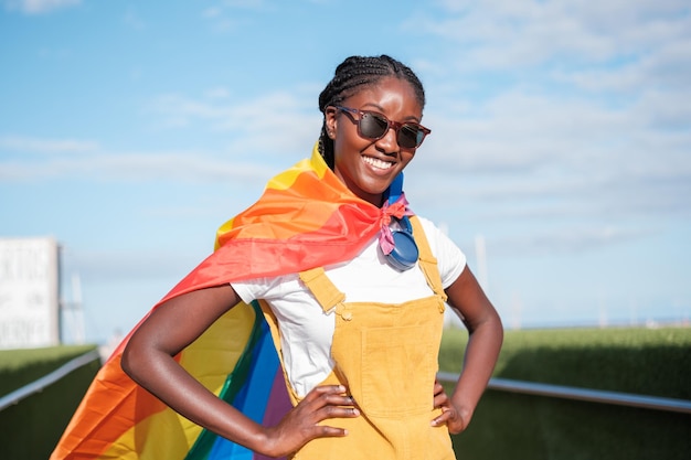 Giovane donna con occhiali da sole che indossa un mantello da supereroe con la bandiera LGBTI Arcobaleno di orgoglio di stile di vita di concetto