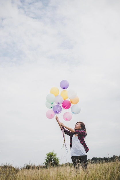 Giovane donna con palloncini colorati sul campo contro il cielo