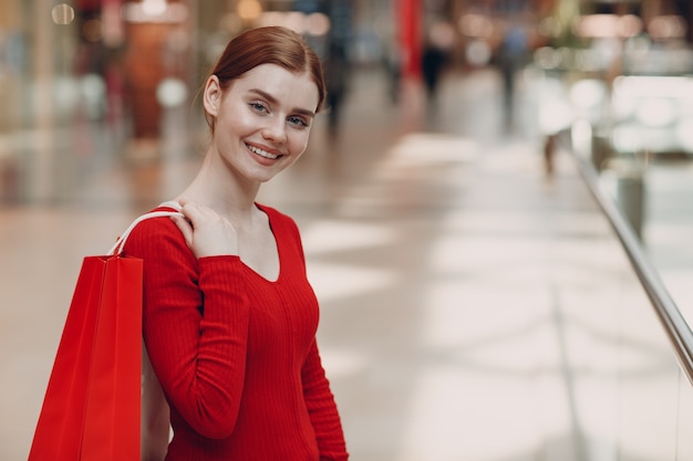 Giovane donna con sacchetti di carta rossa nel centro commerciale. Venerdì nero e concetto di giorno di San Valentino.