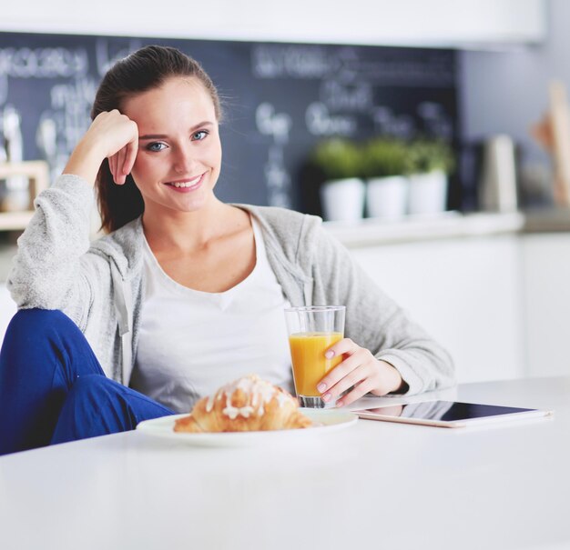 giovane donna con succo d'arancia e tablet in cucina