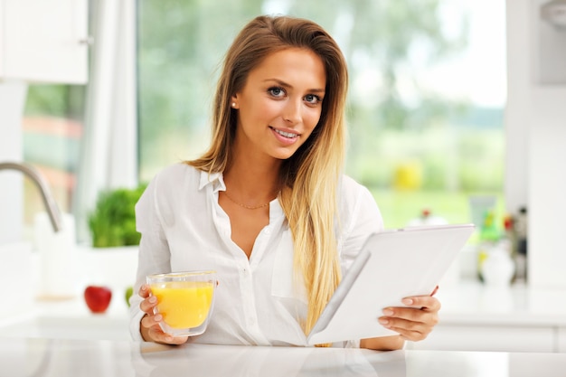 giovane donna con succo d'arancia e tablet in cucina