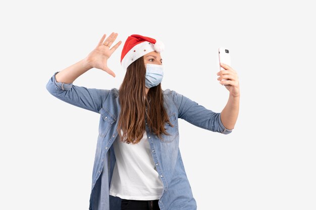 Giovane donna con telefono, mascherina medica e cappello santa. Acquisti natalizi online in quarantena.