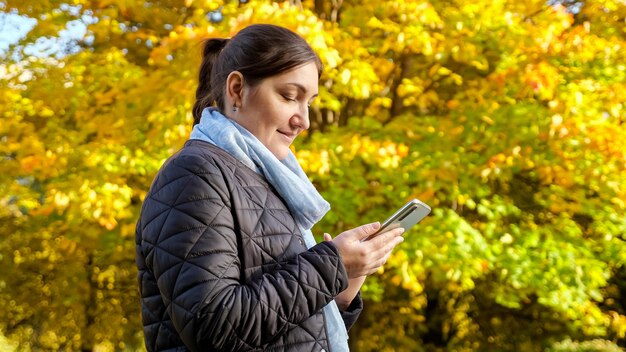 Giovane donna con telefono sullo sfondo di alberi gialli.