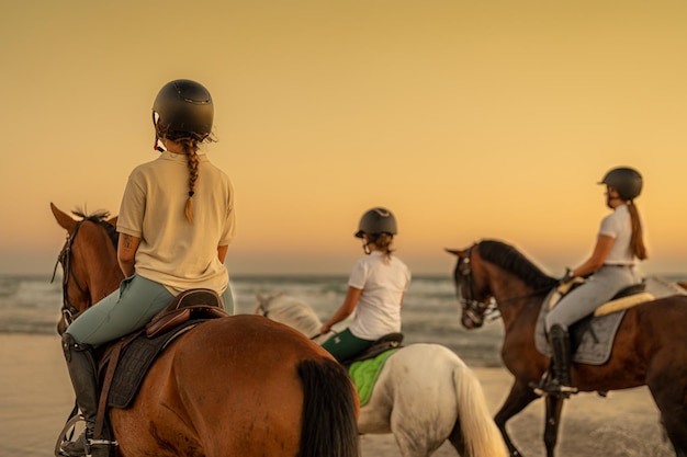 Giovane donna con treccia a cavallo sulla spiaggia accanto a 2 giovani cavalieri