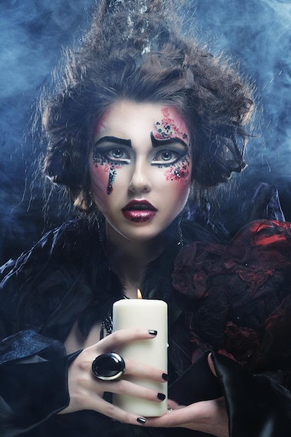 Giovane donna con trucco luminoso che indossa il costume di carnevale che tiene una candela Immagine di Halloween