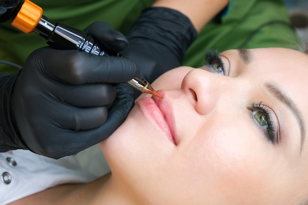 Giovane donna con trucco permanente sulle labbra presso il salone di estetiste. Sfondo verde naturale