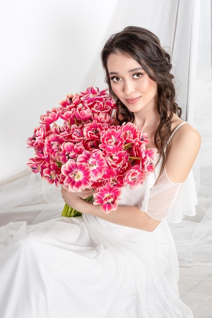 Giovane donna con tulipani rosa in abito bianco mani