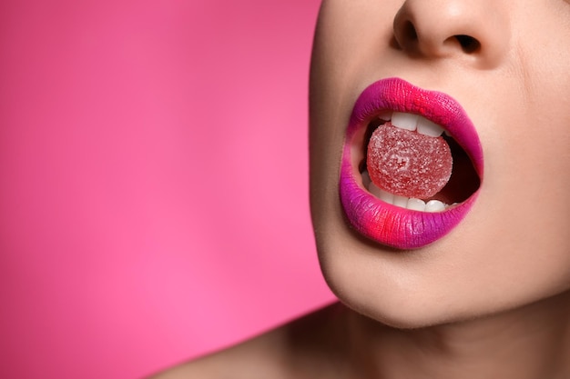 Giovane donna con un bel trucco tenendo la caramella nelle labbra su sfondo rosa primo piano Spazio per il testo