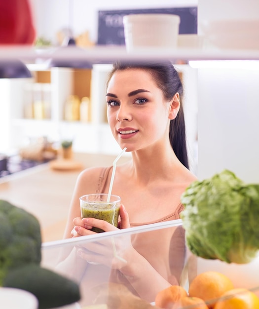 Giovane donna con un bicchiere di gustoso frullato sano a tavola in cucina