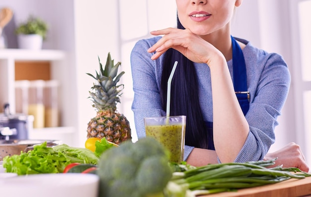 Giovane donna con un bicchiere di gustoso frullato sano a tavola in cucina