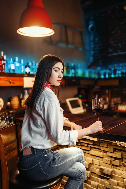 Giovane donna con un bicchiere di vino rosso seduto al bancone del bar in legno. Svaghi femminili del cliente nel pub