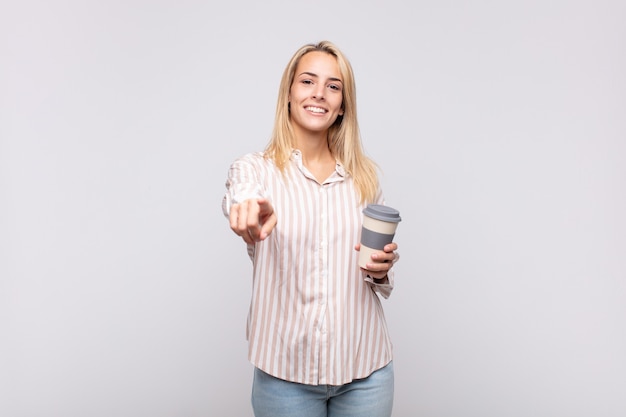 Giovane donna con un caffè che punta alla telecamera con un sorriso soddisfatto, fiducioso e amichevole, scegliendo te