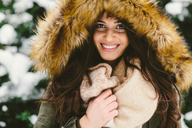 Giovane donna con un cappuccio di pelliccia nel parco sulla neve