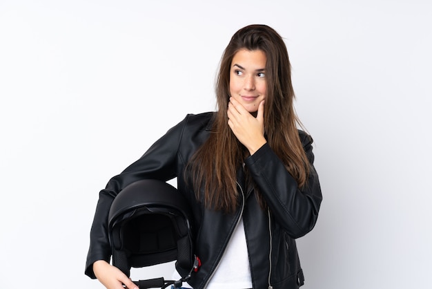 Giovane donna con un casco del motociclo sopra la parete bianca isolata che pensa un'idea