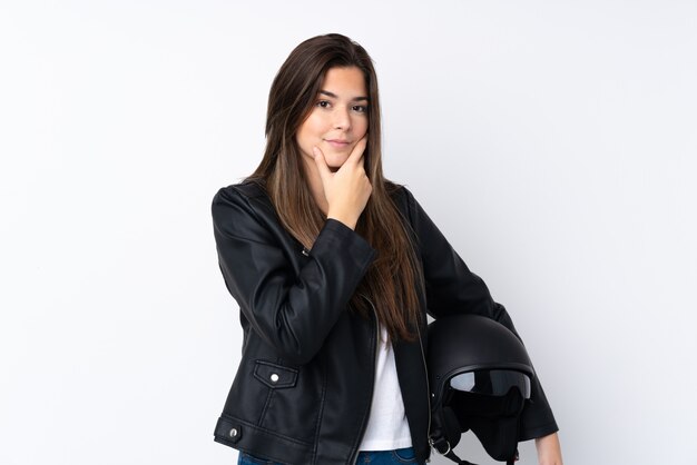 Giovane donna con un casco del motociclo sopra la parete bianca isolata che pensa un'idea