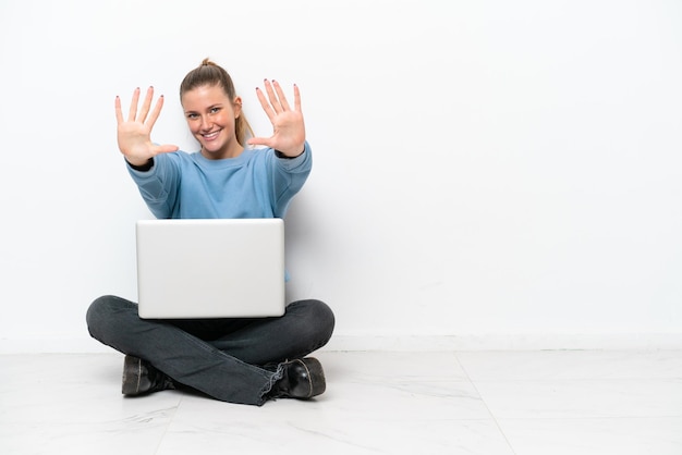 Giovane donna con un computer portatile che si siede sul pavimento che conta dieci con le dita