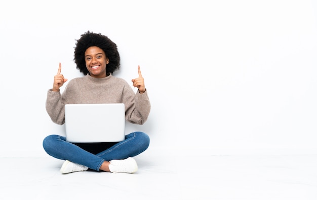 Giovane donna con un computer portatile che si siede sul pavimento che indica una grande idea