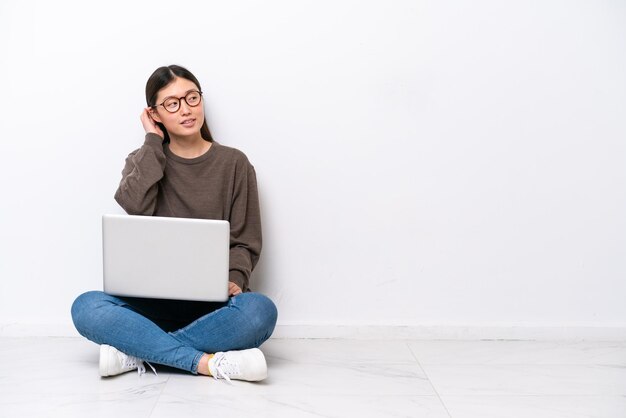 Giovane donna con un computer portatile che si siede sul pavimento che pensa un'idea