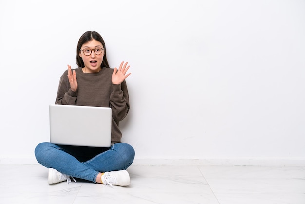 Giovane donna con un computer portatile che si siede sul pavimento con l'espressione facciale di sorpresa