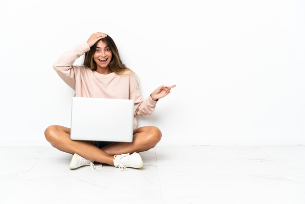 Giovane donna con un computer portatile che si siede sul pavimento isolato