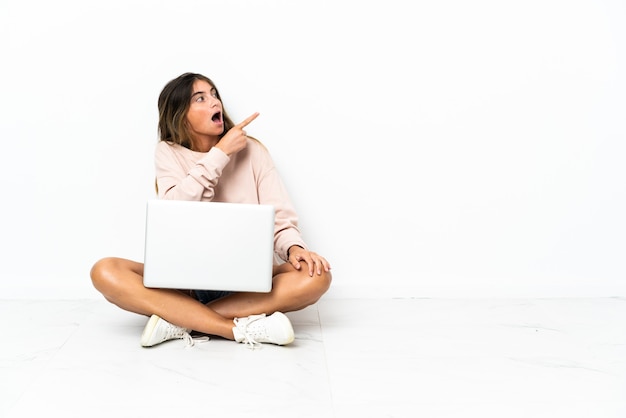 Giovane donna con un computer portatile che si siede sul pavimento isolato