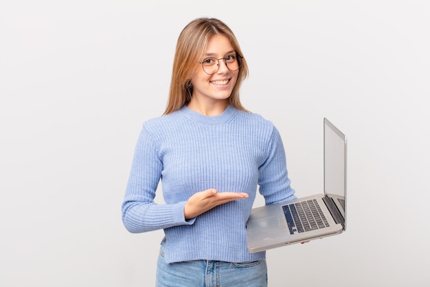 Giovane donna con un computer portatile che sorride allegramente, si sente felice e mostra un concetto