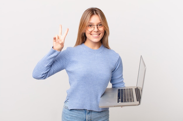 Giovane donna con un computer portatile che sorride e sembra amichevole, mostrando il numero due