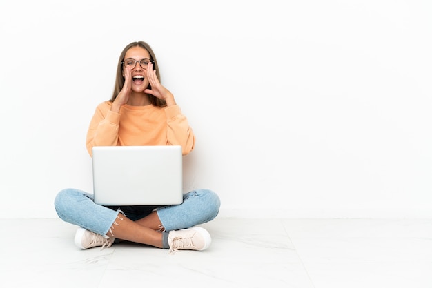 Giovane donna con un computer portatile seduta sul pavimento che grida e annuncia qualcosa
