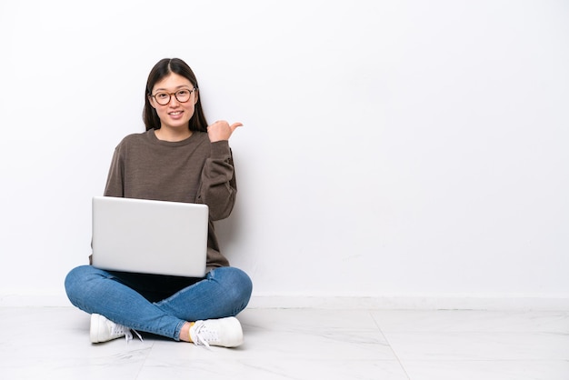 Giovane donna con un computer portatile seduto sul pavimento che punta verso il lato per presentare un prodotto