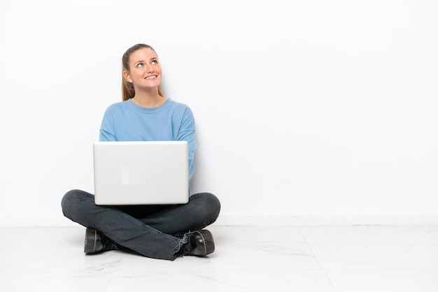 Giovane donna con un computer portatile seduto sul pavimento guardando in alto mentre sorride