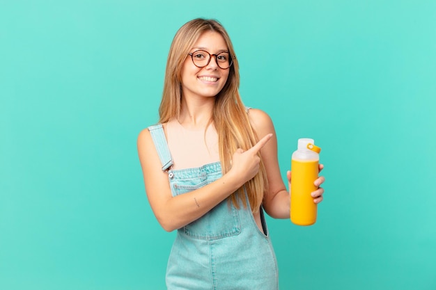 Giovane donna con un frullato che sorride allegramente, si sente felice e indica il lato